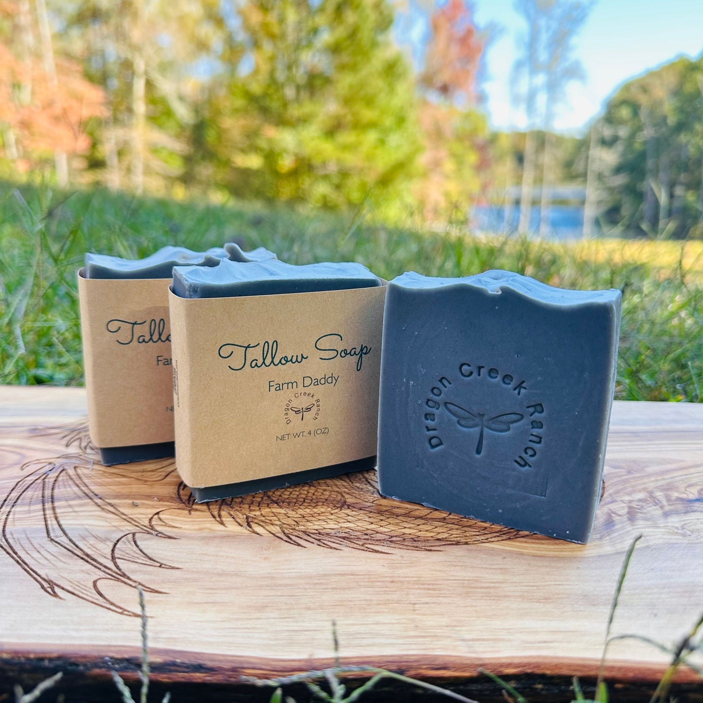 Three bars of dark grey Farm Daddy Tallow Soap on a wooden surface with a natural background.