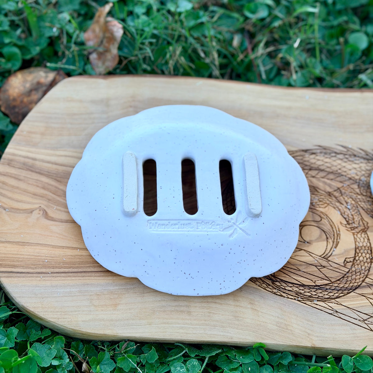 Underside of a white speckled soap tray showing raised feet and the Wanderlust Pottery dragonfly stamp