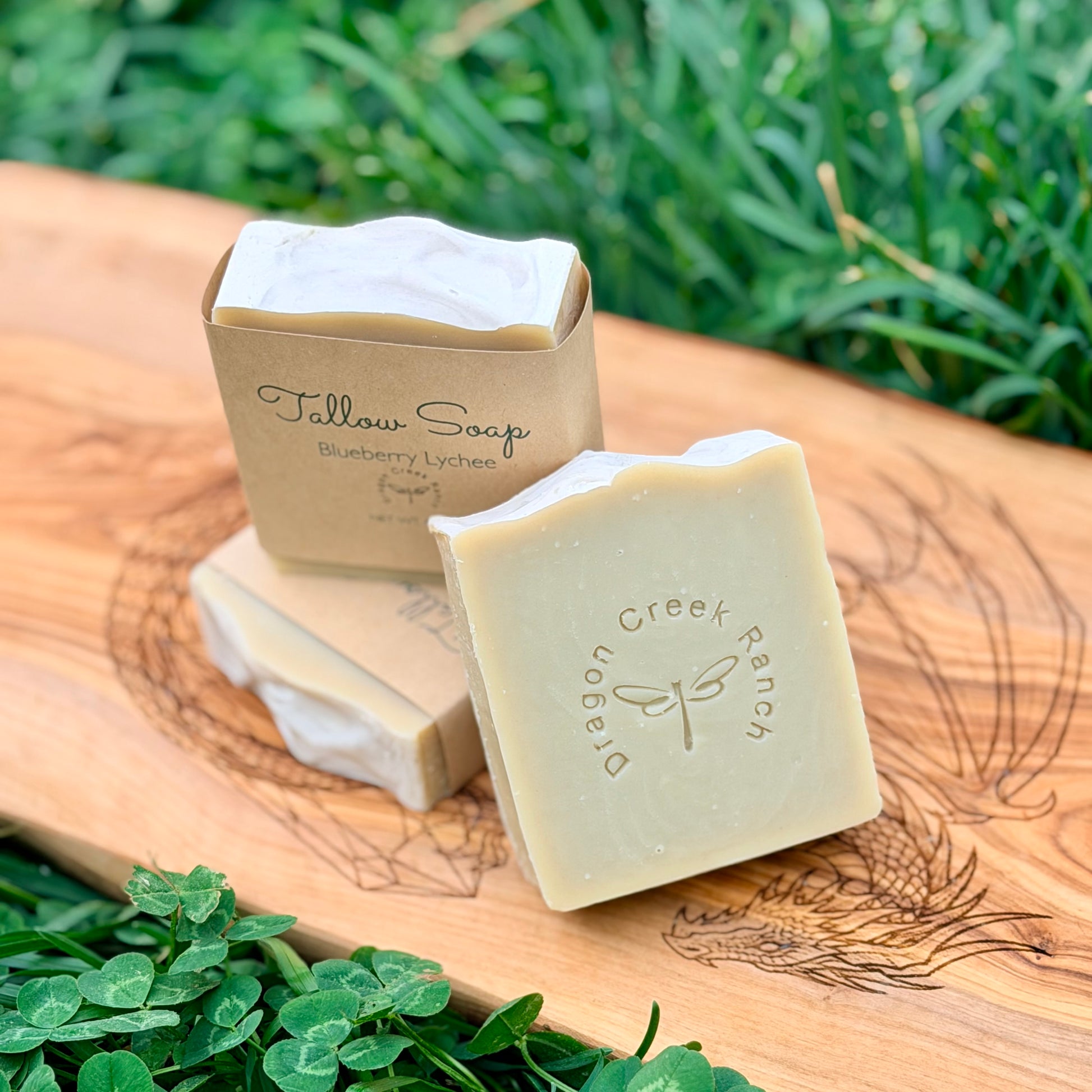 Three bars of soap and a box on a wooden board with grass in the background