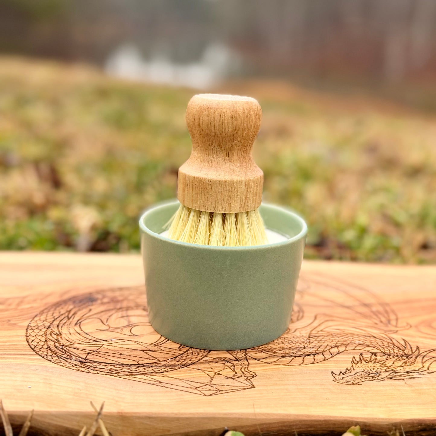 Green ceramic cup with wooden brush on a wooden surface outdoors