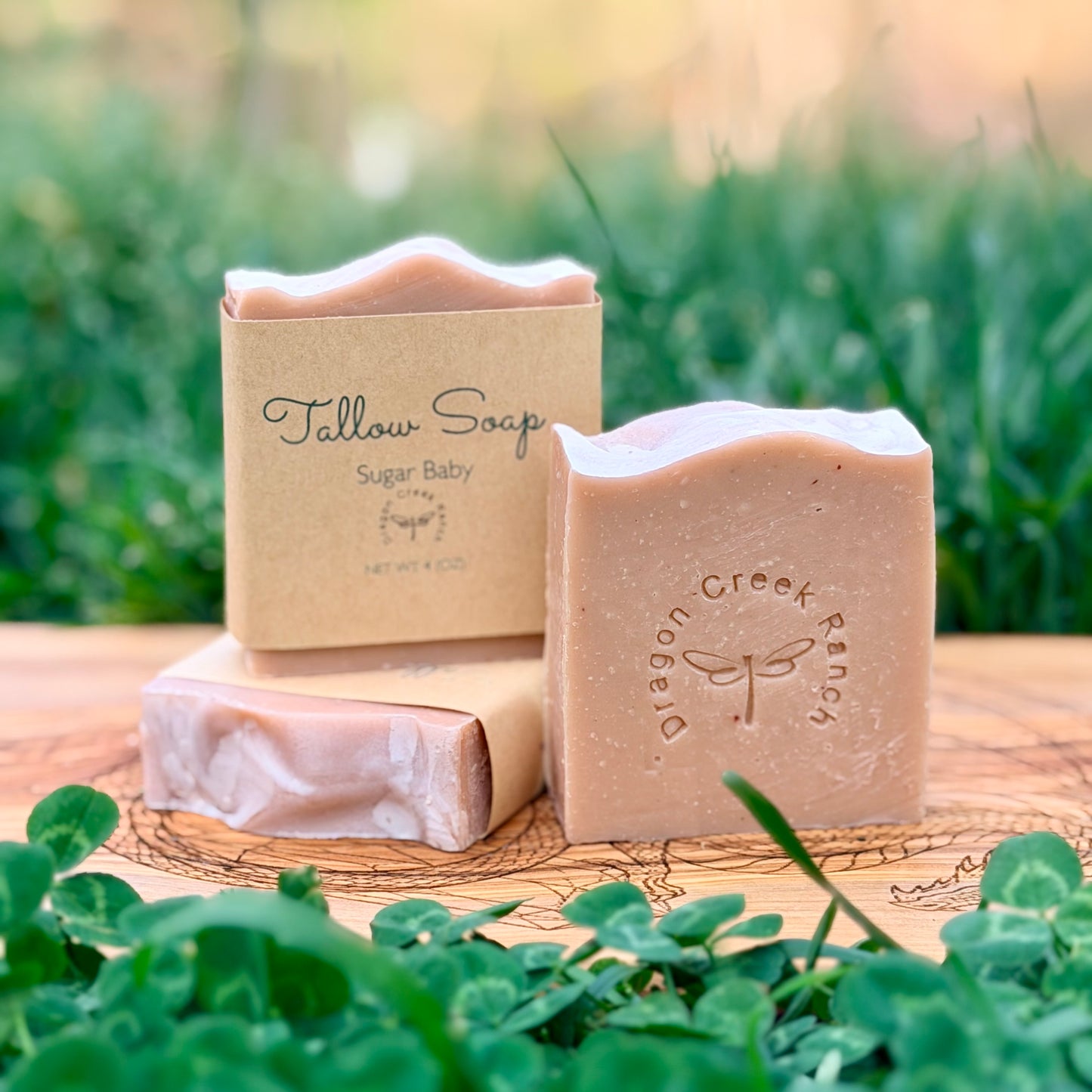 Three bars of soap and a box labeled 'Tallow Soap' on a wooden surface with a natural background.