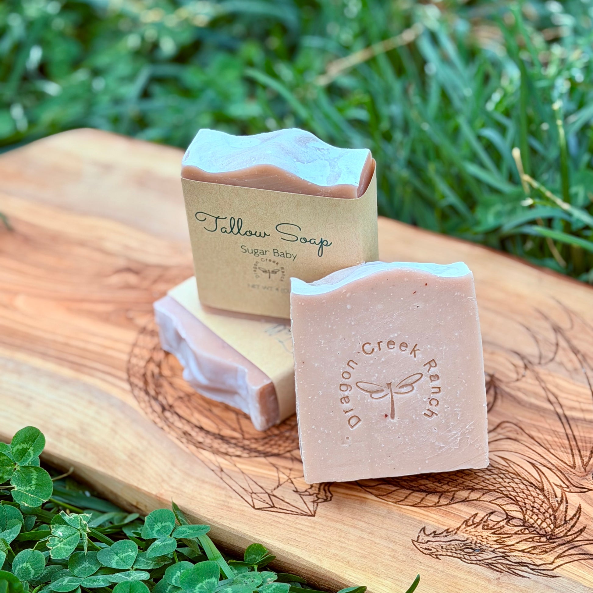 Three bars of pink Sugar Baby soap on a wooden board with grass in the background