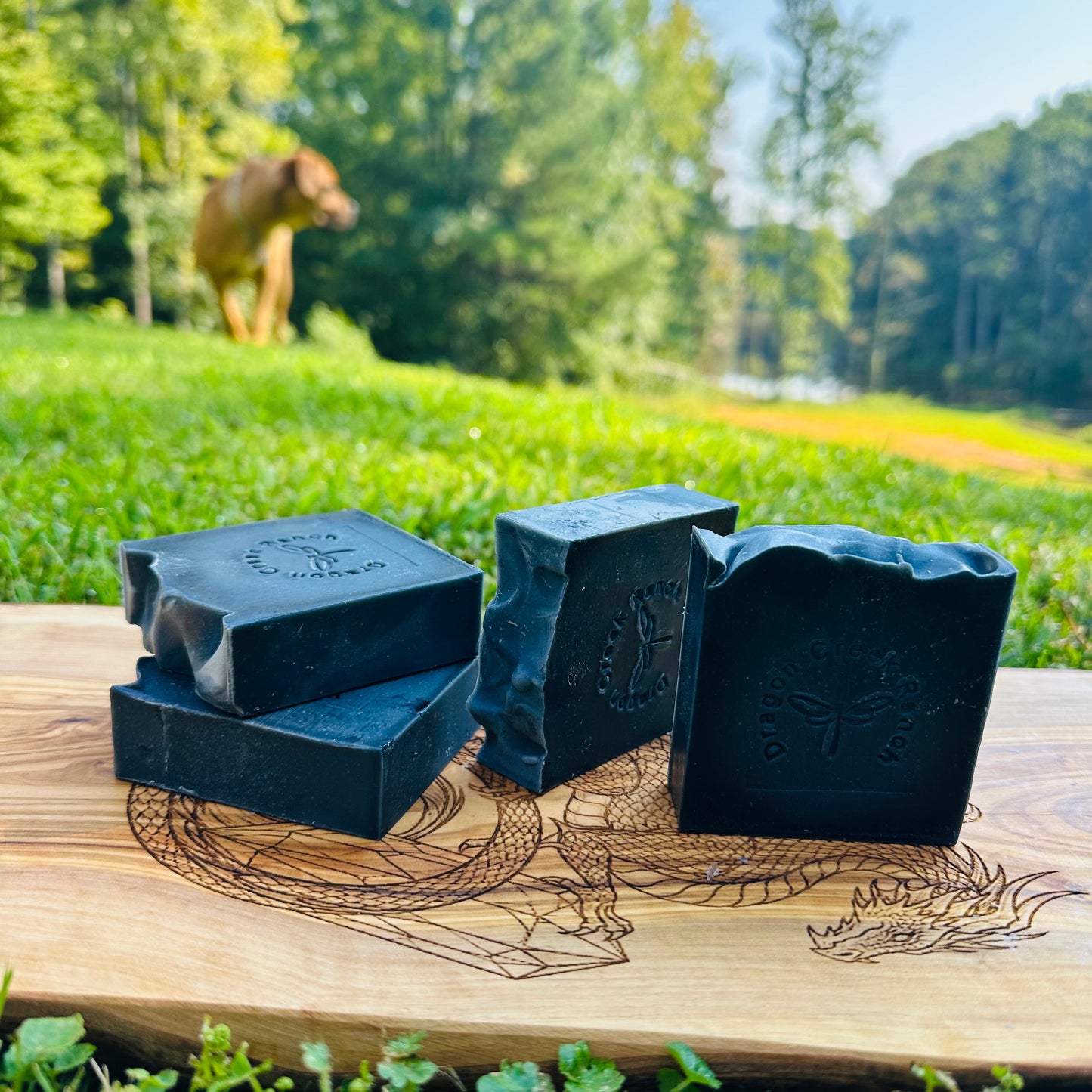Four black soap bars on a wooden board with a natural outdoor background