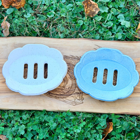 White and blue scalloped handmade pottery soap trays with three drain slots, top view on a dragon engraved board