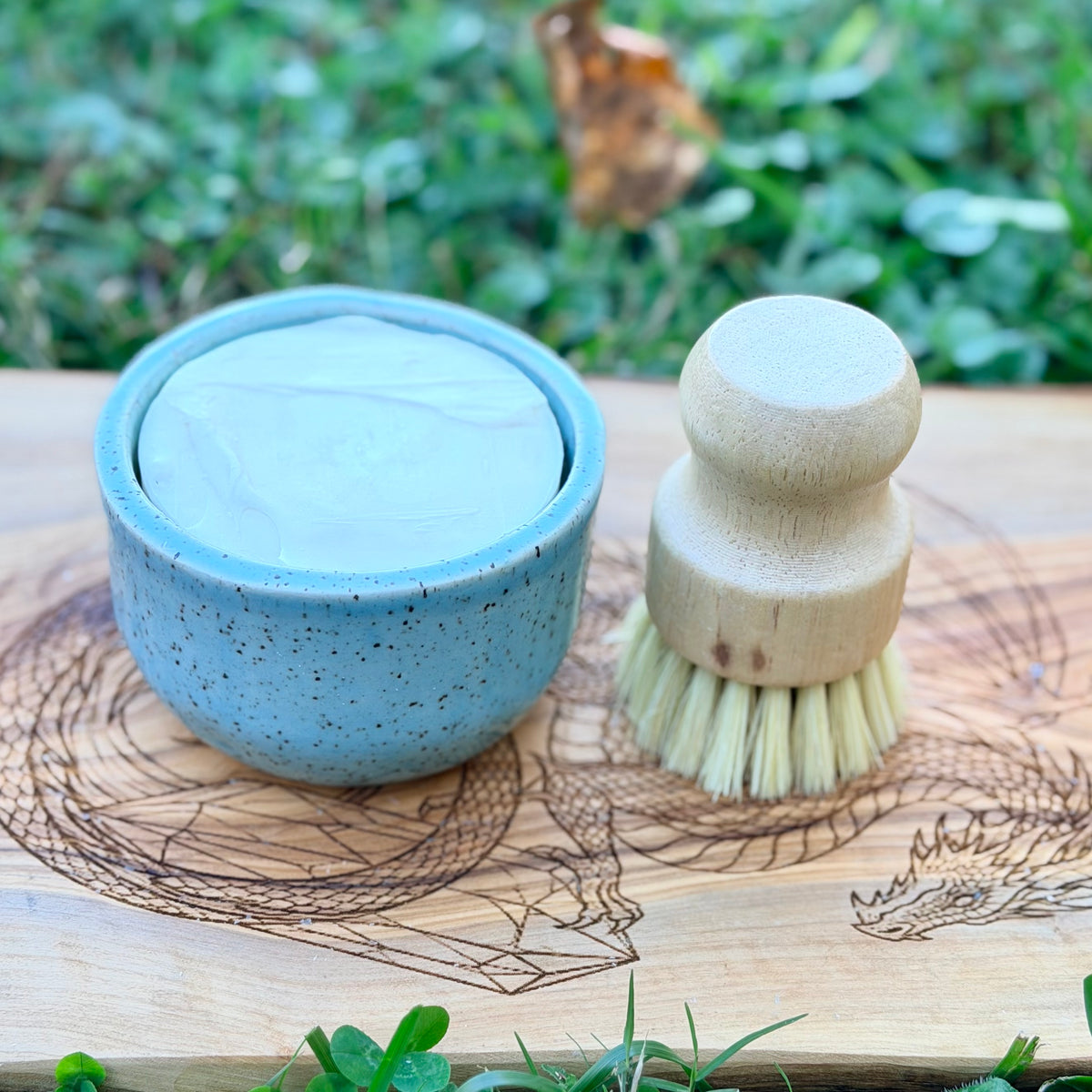 Blue speckled ramekin filled with a white tallow dish soap puck, with a wooden dish brush beside it