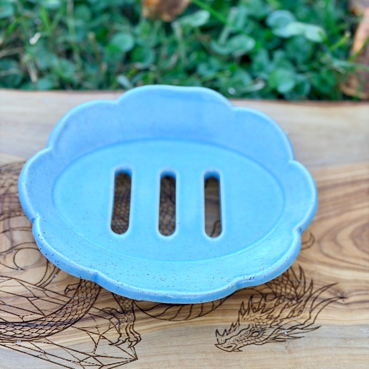 Blue speckled scalloped handmade pottery soap tray with three drain slots on a dragon engraved wood board