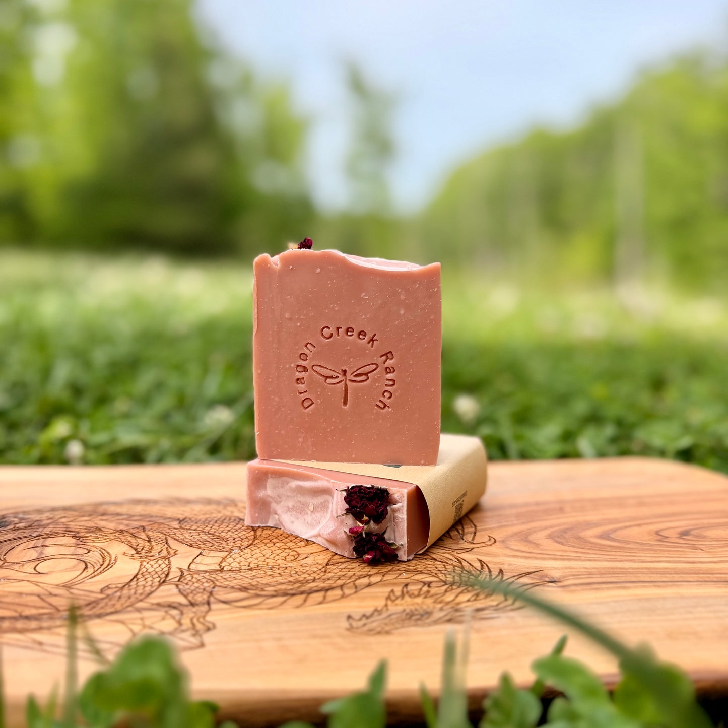 Two Bars of pink soap with dried roses on a wooden board outdoors