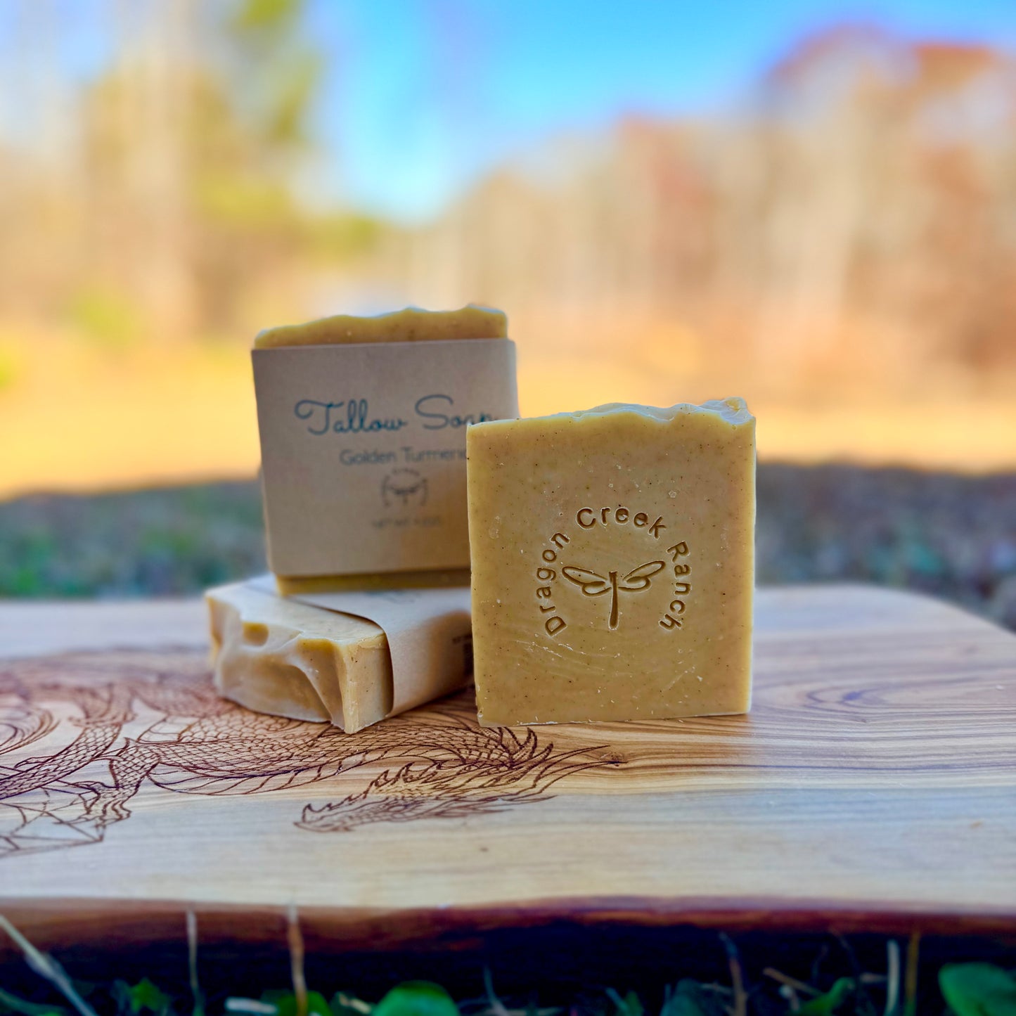 Three bars of soap with 'Dragon Creek Ranch' branding on a wooden surface outdoors.