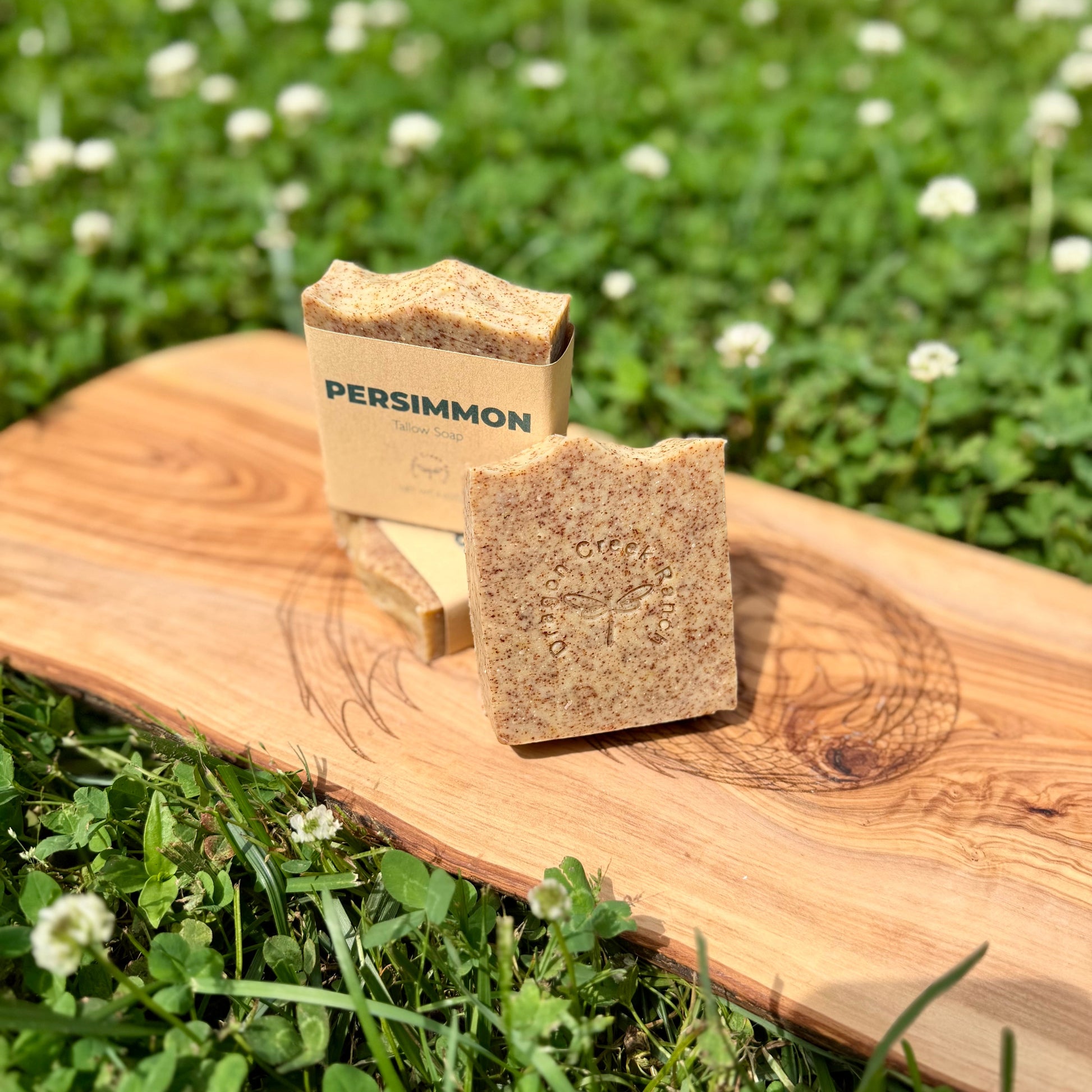 Three bars of Persimmon soap on a wooden board with a grassy background