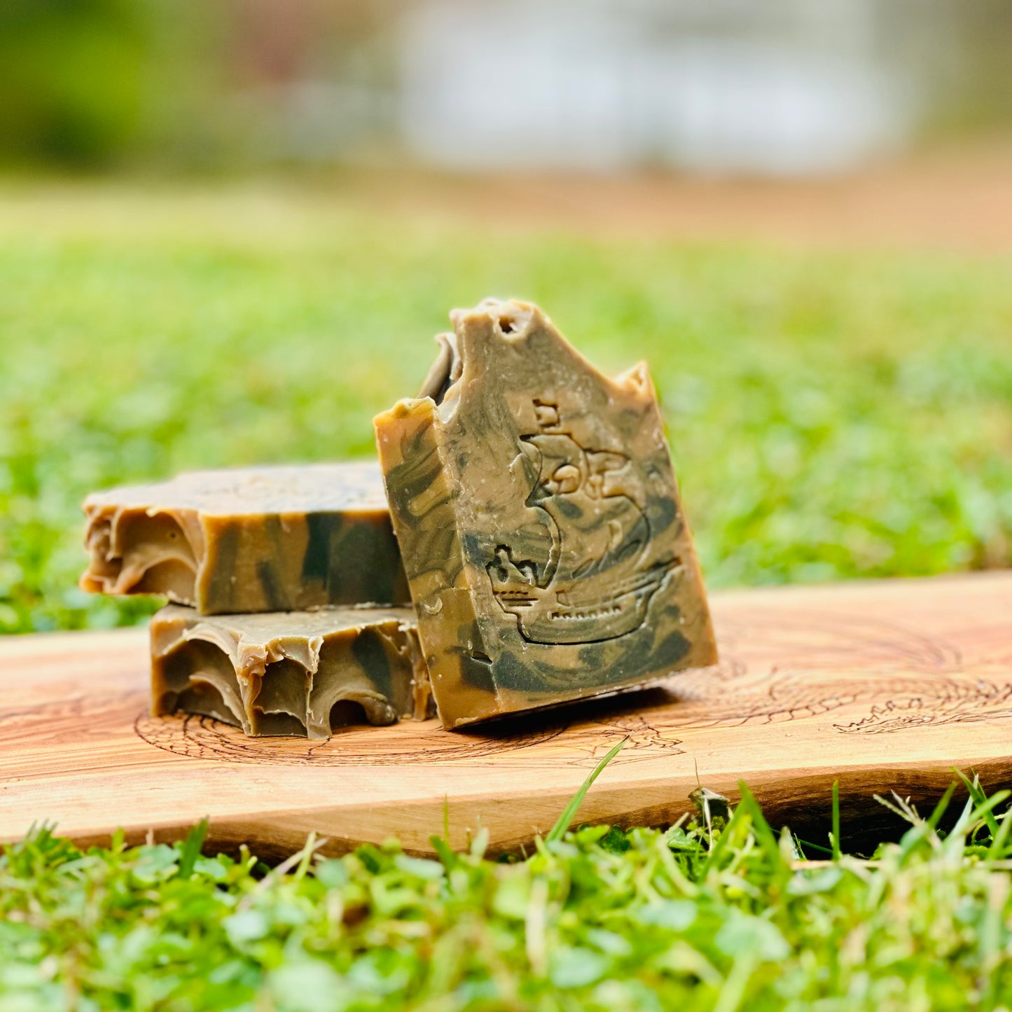 Three soap bars with a ship design on a wooden board outdoors.