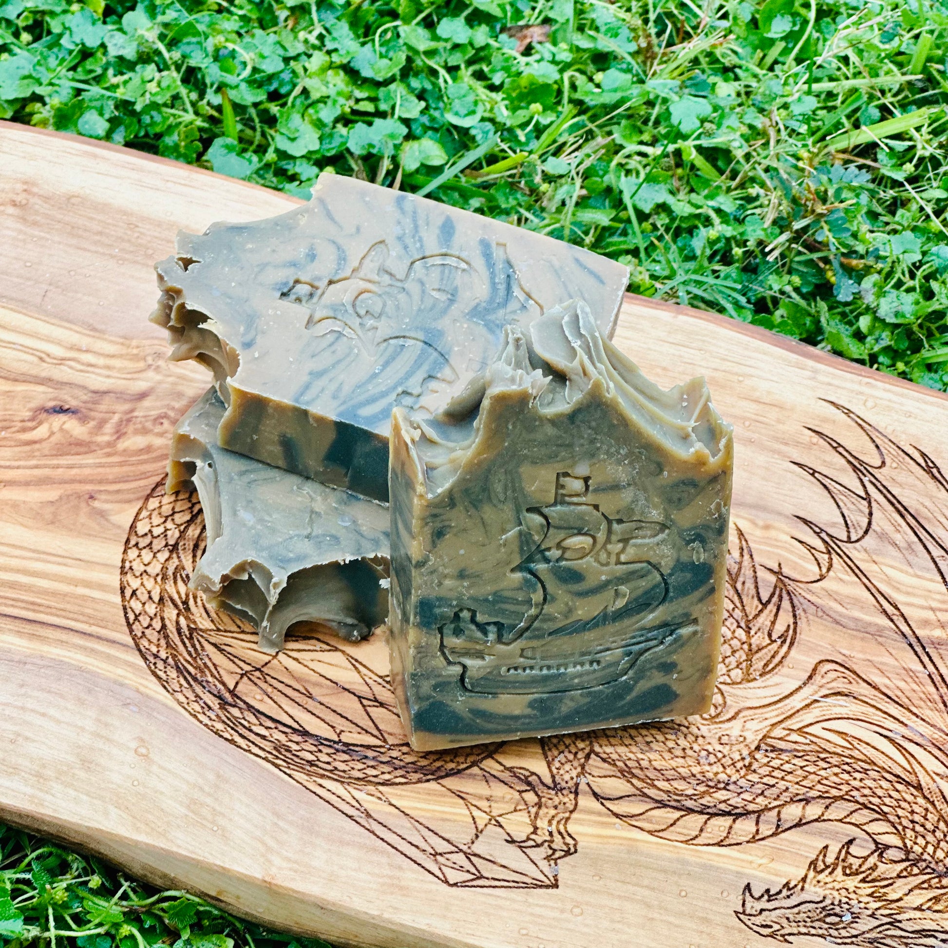 Two pieces of soap with engraved designs on a wooden board outdoors.