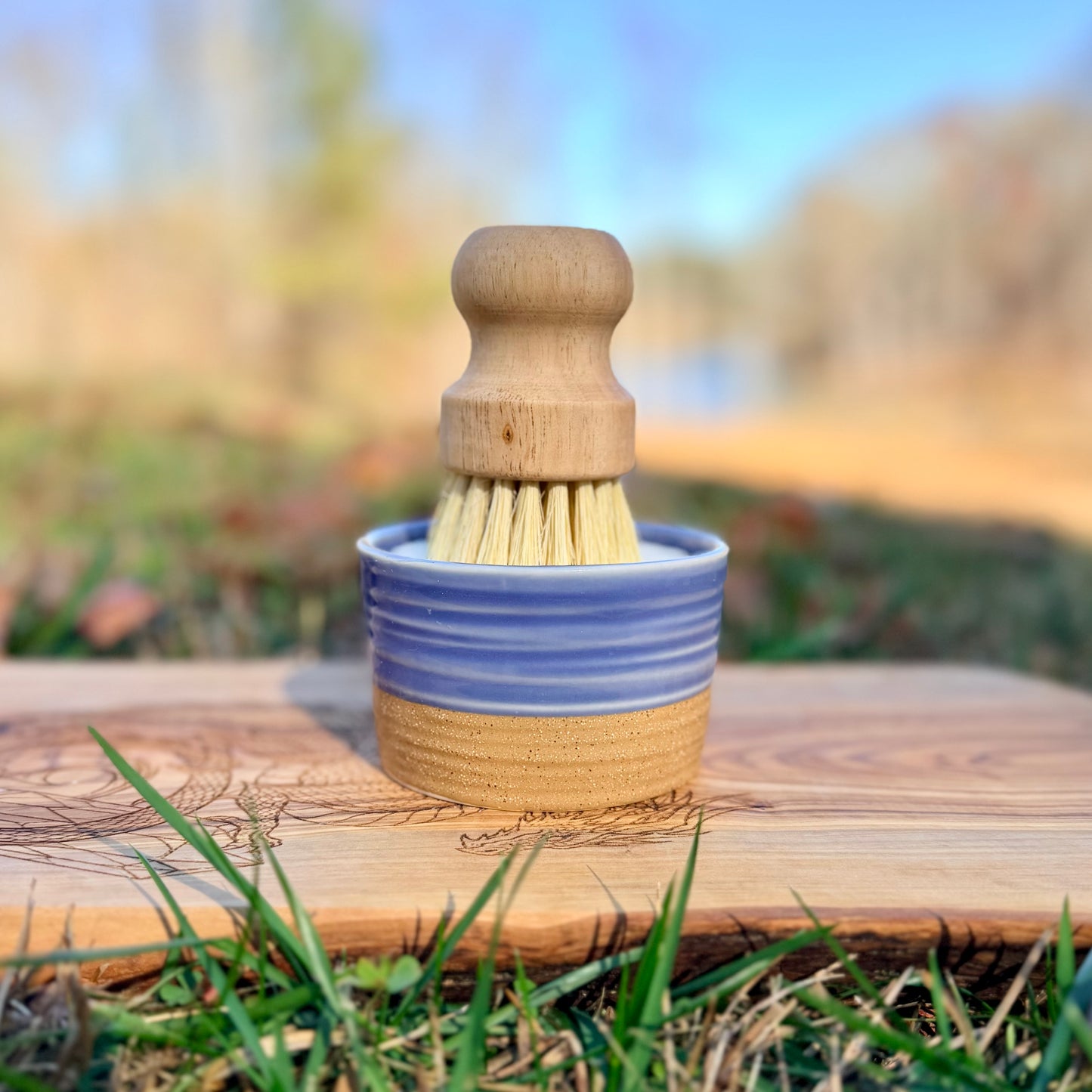 Wooden brush in a blue and brown ramekin on a wooden surface with a natural background