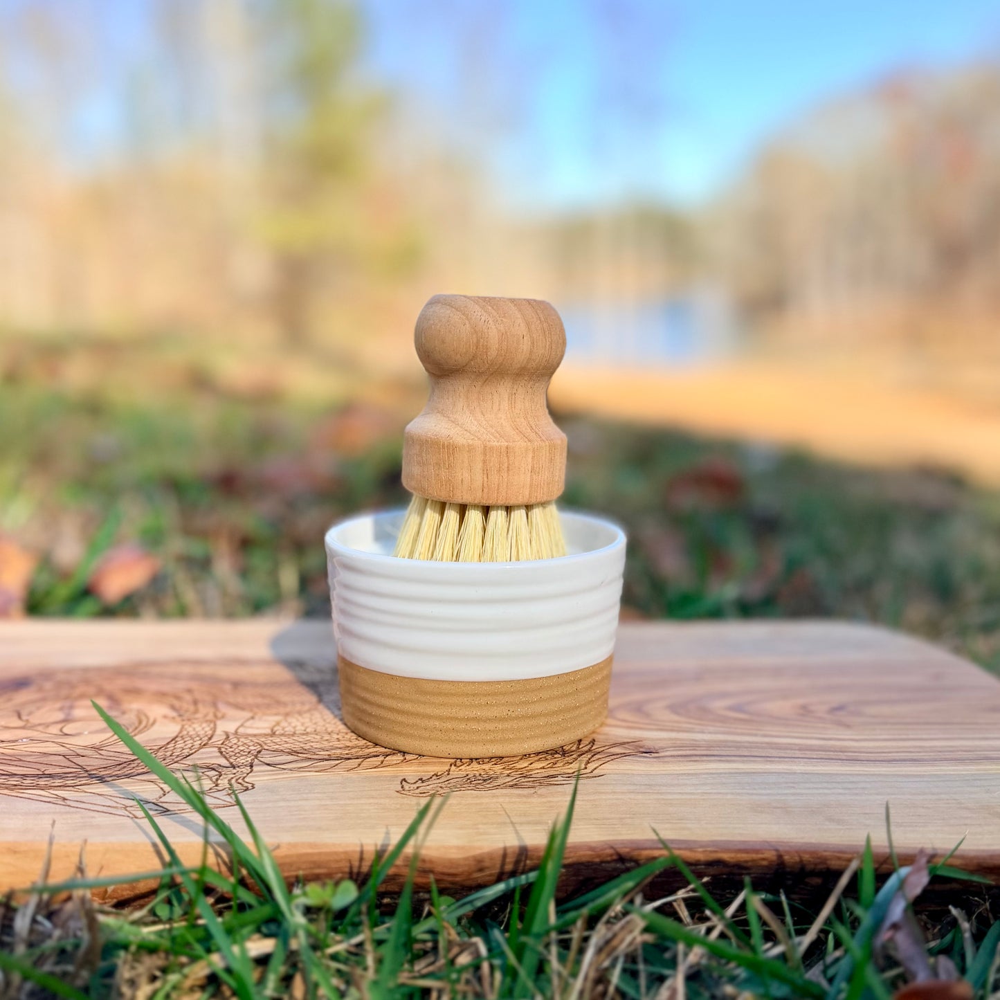 Wooden brush in a white and beige ramekin on a wooden surface outdoors.