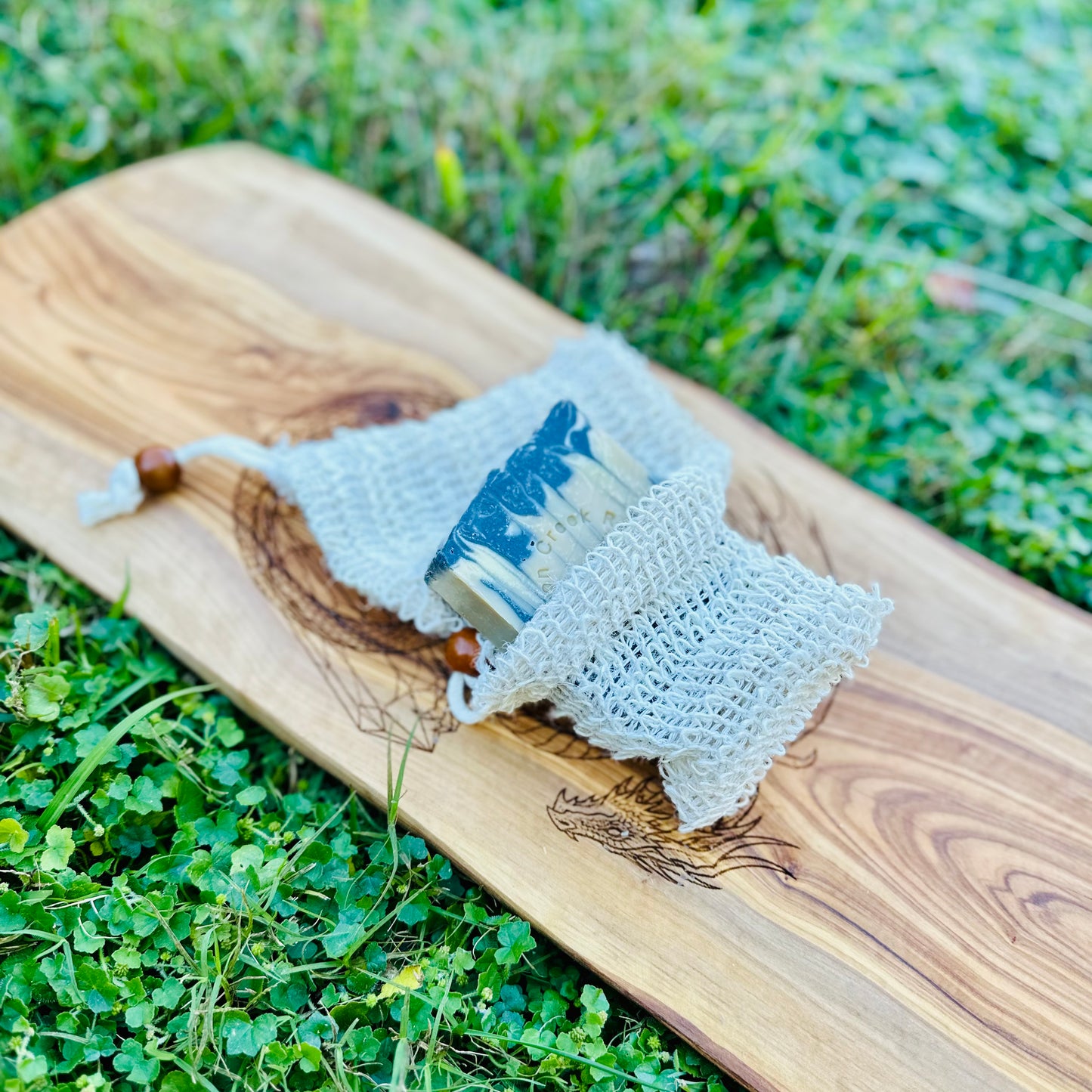 Bar of soap in a mesh bag on a wooden board with grass in the background