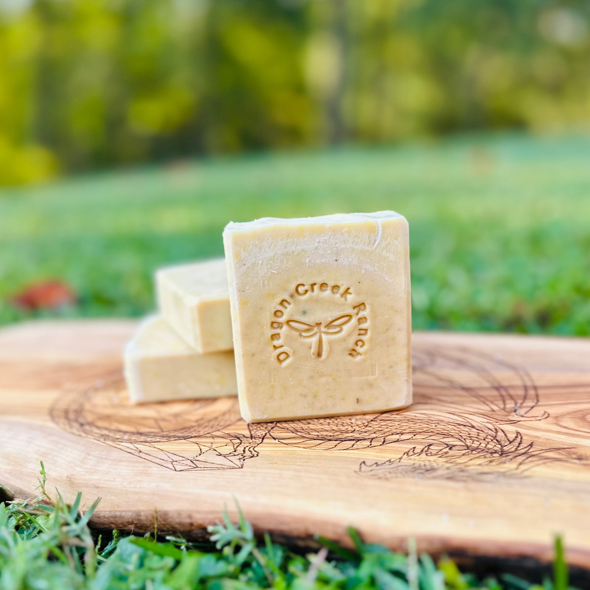 Three bars of soap on a wooden board with 'Dragon Creek Ranch' branding, outdoors.