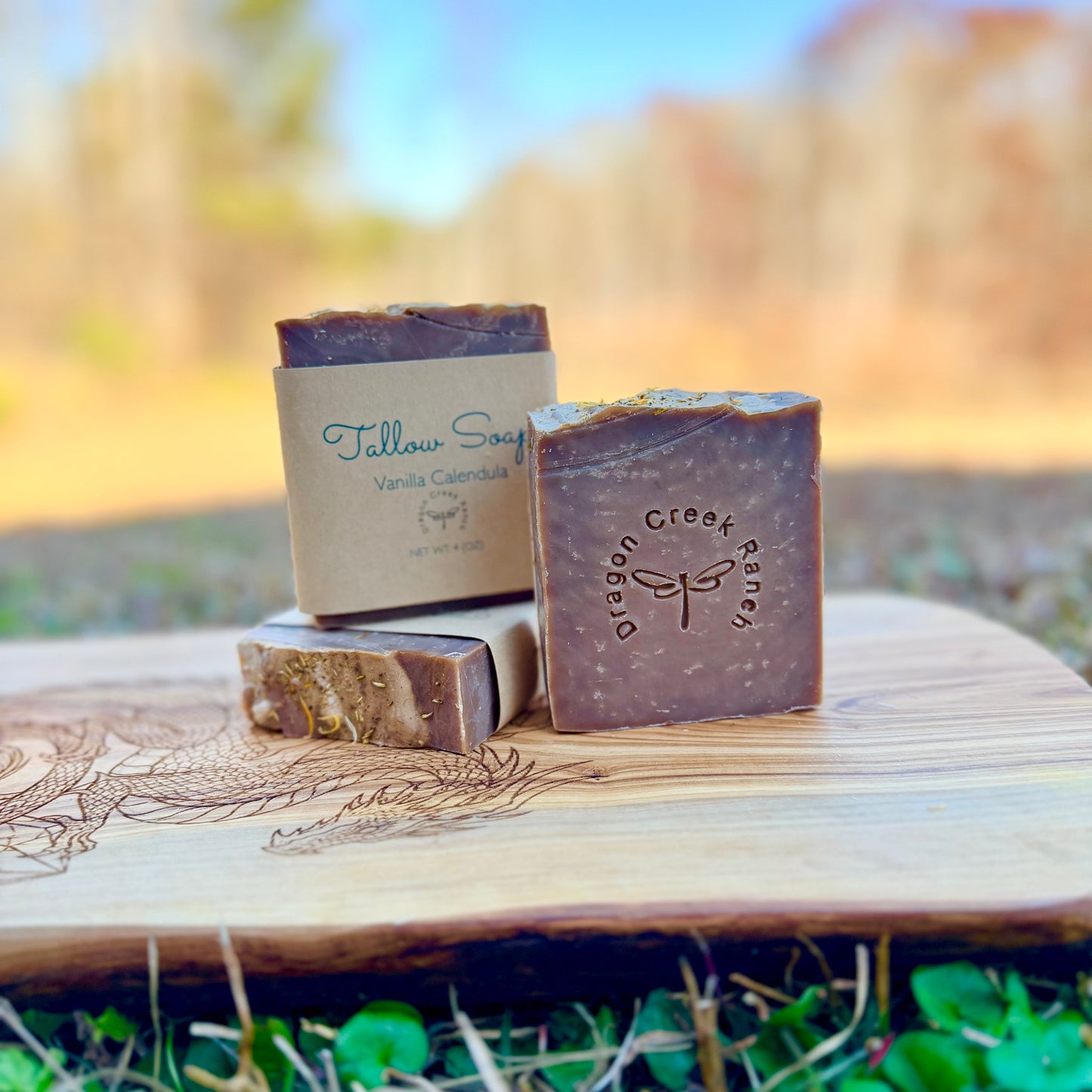Three bars of soap with 'Dragon Creek Ranch' branding on a wooden surface outdoors.