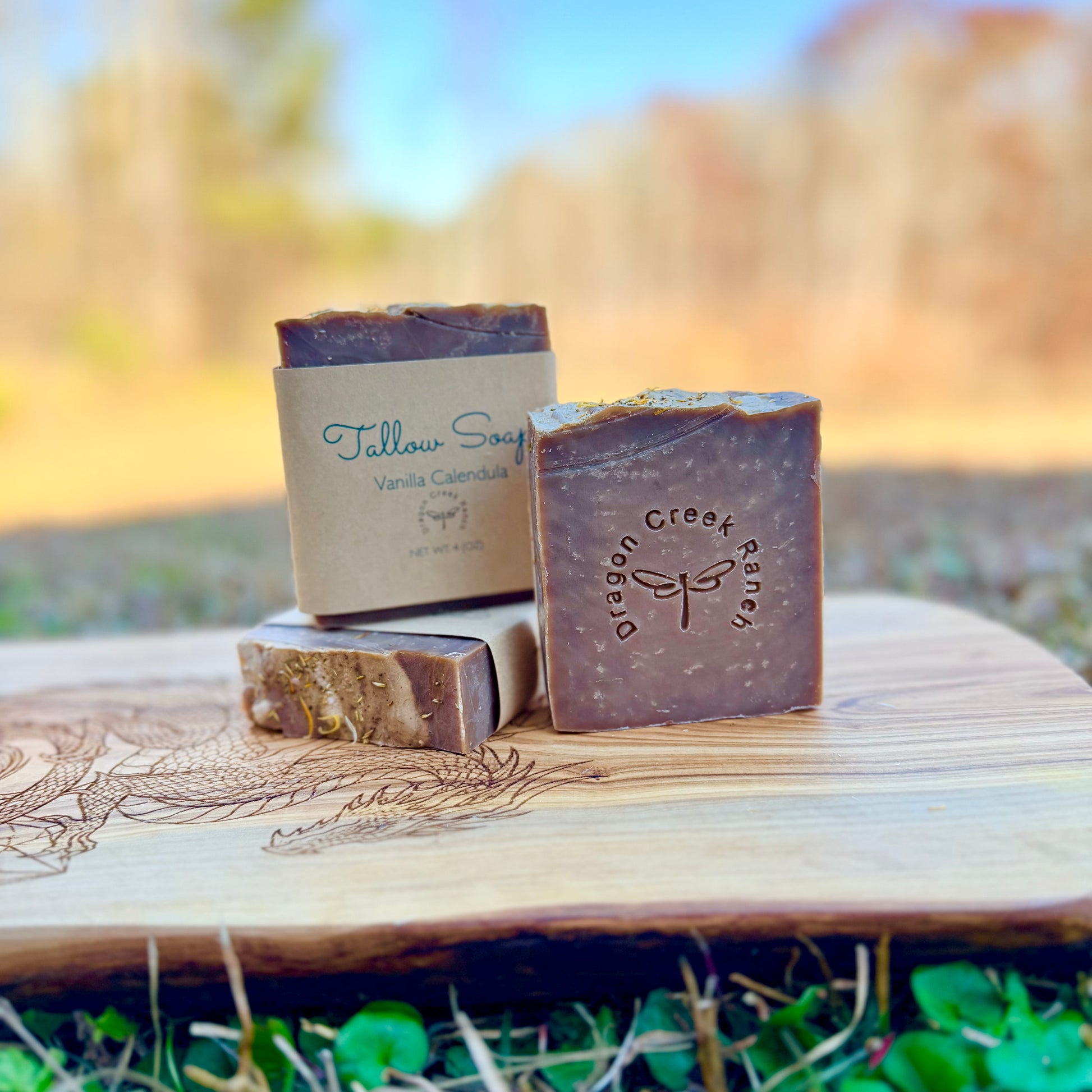 Three bars of soap with 'Dragon Creek Ranch' branding on a wooden surface outdoors.