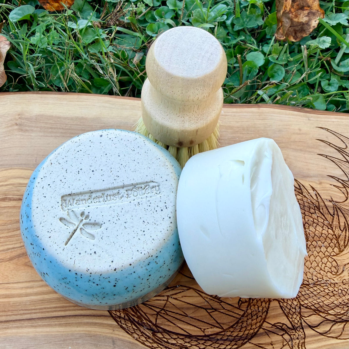 Bottom of a blue speckled ramekin with the Wanderlust Pottery dragonfly stamp, beside a white tallow dish soap puck