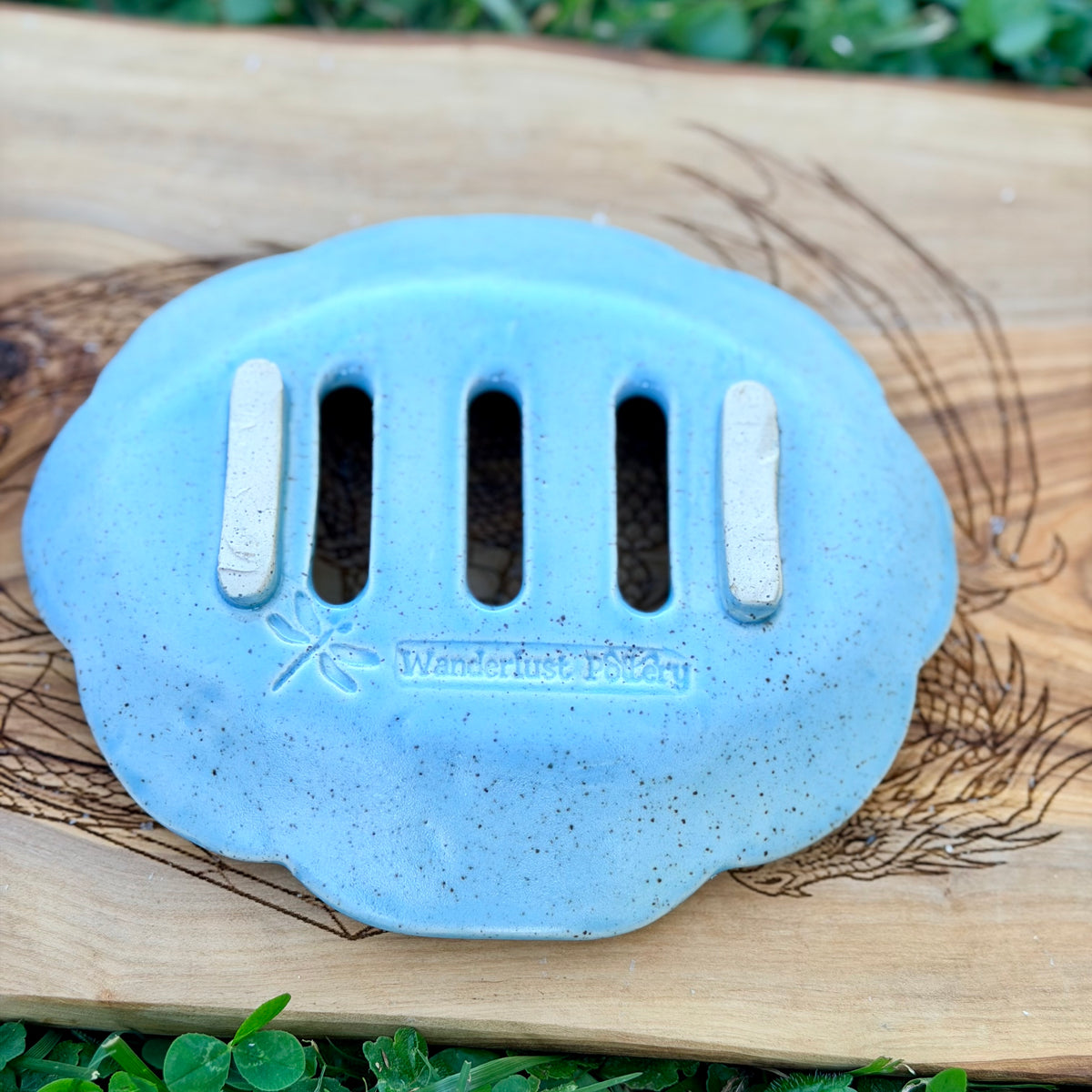 Underside of a blue speckled soap tray showing raised feet and the Wanderlust Pottery dragonfly stamp
