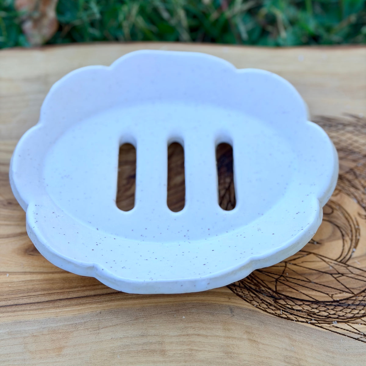 White speckled scalloped handmade pottery soap tray with three drain slots on a wood board